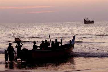 Malpe sahilinde balıkçı teknesi ve balıkçıların balık yüklediği renkli günbatımı; Arap denizi; Udupi; Karnataka; Hindistan