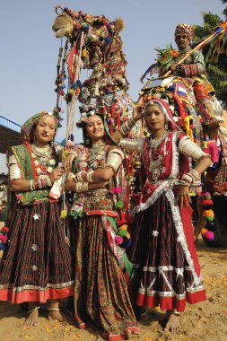 Geleneksel mücevher ve rajasthani kostümlü kızlar Pushkar Fair, Rajasthan, Hindistan 'da süslü devenin önünde duruyorlar.  