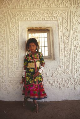 Tavşanın çamurlu duvarlarına karşı duran kız - kulübe, Kutch, Gujarat, Hindistan 