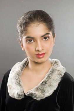 Gri arka planda kürklü yakalı genç Hintli kadın. 