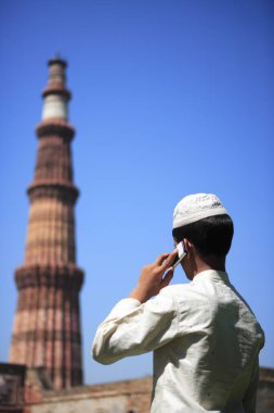 Kutub Minar 'da cep telefonuyla konuşan Müslüman çocuk 1311 kırmızı kumtaşı kulesinde inşa edilmiş; Hint-Müslüman sanatı; Delhi sultanlığı; Delhi; Hindistan UNESCO Dünya Mirası Sitesi