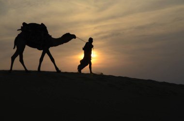 Hindistan 'da Jaisalmer' de gün batımında deve ve insan kum tepesinde yürüyor.