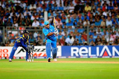 Hintli vurucu M S Dhoni atışını yaparken, Sri Lankalı kaptan kaleci Kumar Sangakkara Hindistan ile Sri Lanka arasındaki ICC Dünya Kupası finalinde 2 Nisan 2011 'de Wankhede Stadyumu' nda görülüyor.