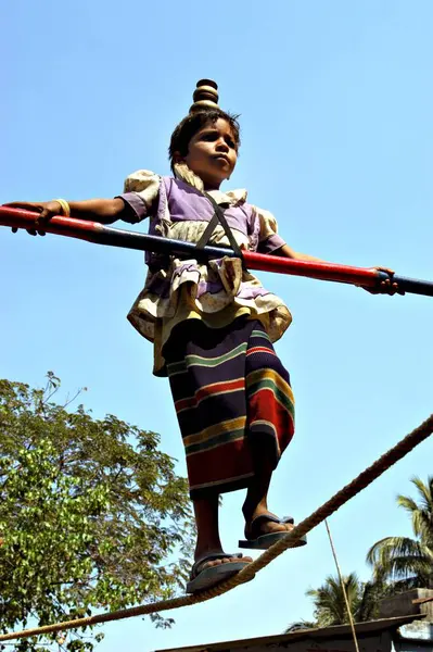 Güney Asyalı kız sokak sanatçısı elinde bambuyla ipte yürüyerek dengede duruyor. Gösteriden sonra çocuğun ailesi Bombay, Maharashtra, Hindistan 'daki insanlardan para topluyor. 