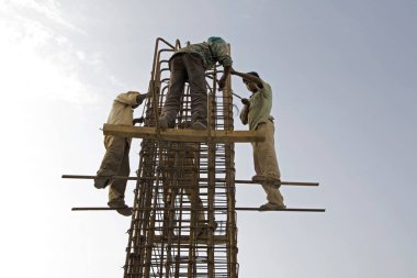 İşçiler emniyet kemerleri ve kaskları olmadan ayakta duruyor ve Ahmedabad, Gujarat, Hindistan 'da bir inşaat alanında çalışıyorlar.