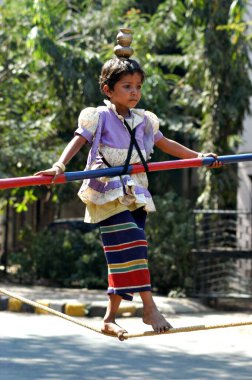 Güney Asyalı kız sokak sanatçısı elinde bambuyla ipte yürüyerek dengede duruyor. Gösteriden sonra çocuğun ailesi Bombay, Maharashtra, Hindistan 'daki insanlardan para topluyor..