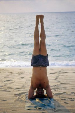 Hintli adam kumlu sahilde yoga yapıyor.