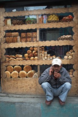 Man talking on mobile phone outside bakery, Kargil, Leh, Ladakh, Jammu and Kashmir, India  10 April 2008  clipart