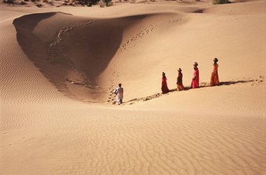 Rajasthani kadınları su kabı taşır ve adam kumlarda davul çalar, Khuhri, Jaisalmer, Rajasthan, Hindistan 