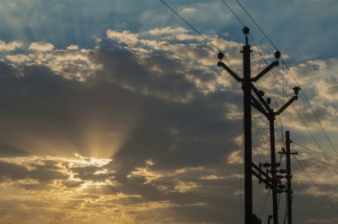 Günbatımında gökyüzüne karşı kablolu elektrik iletim kuleleri 