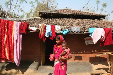 Hindistanda Jharkhand 'daki geleneksel çamurlu evin önünde çocuklu bir kadın duruyor.   