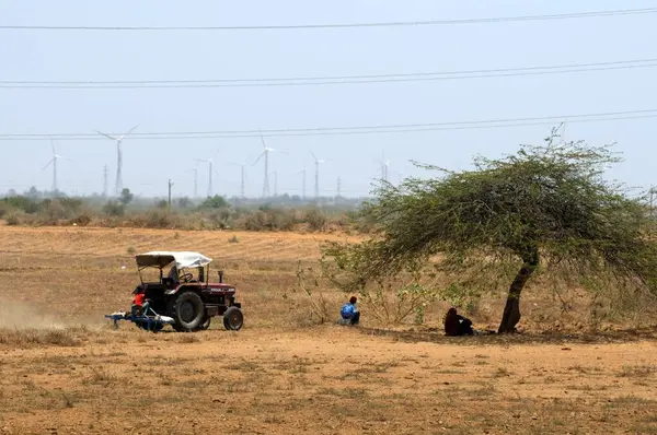 Arkasında yel değirmenleri olan kuru alanda traktör; Kutch; Gujarat; Hindistan