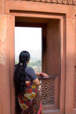 Agra kırmızı kale penceresinden dışarı bakan uzun saçlı bir bayan; Uttar Pradesh; Hindistan