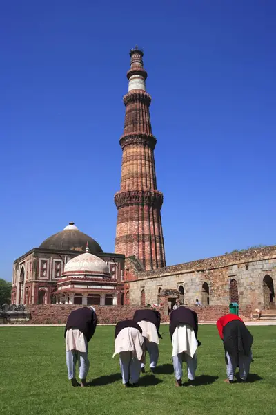 stock image Children doing Namaz in front of Alai Darwaza, Imam Zamin's tomb and Qutab Minar built in 1311 red sandstone tower, Indo-Muslim art, Delhi sultanate, Delhi, India UNESCO World Heritage Site 