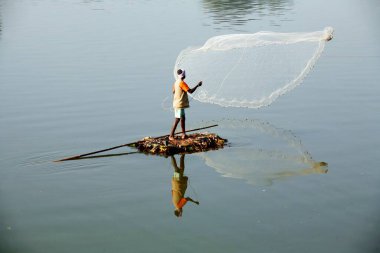 Sangli, Maharashtra, Hindistan 'da Krishna nehrinde balık yakalamak için balıkçı ağlarını attığı derme çatma bir tekneyle Haripur köyünden bir balıkçı.