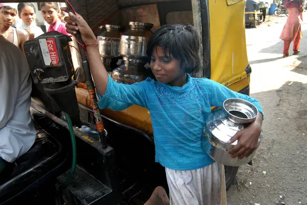 Genç bir kız Chembur, Bombay, Mumbai, Maharashtra, Hindistan 'da bir gecekondu mahallesinde çekçekçekte paslanmaz çelik kaplarda su içiyor. 