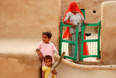 Gobar ya da sığır gübresi kulübesinde çocuklu Rajasthani kadını tuhaf bir şekilde bakıyor, Khuhri, Jaisalmer, Rajasthan, Hindistan   