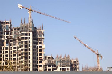 Modern teknoloji vinçleri, güvenlik önlemleri ağları, miğferli inşaat ekibi vs. kullanan çok katlı inşaat kuleleri.