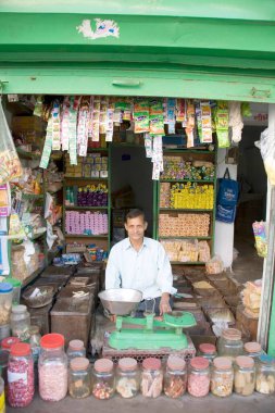 Ağırlık ölçeğinin önünde oturan küçük bir kırsal dükkan sahibi Dilwara, Udaipur, Rajasthan, Hindistan 