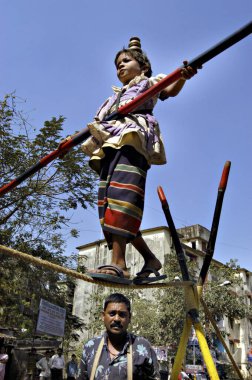 Güney Asyalı kız sokak sanatçısı elinde bambuyla ipte yürüyerek dengede duruyor; performanstan sonra çocuğun ailesi Bombay, Maharashtra ve Hindistan 'da yaşayan insanlardan para topluyor.