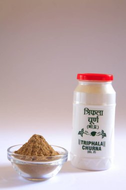 Kronik kabızlıktan kurtulmak için Ayurvedic ilaç triphala churna tozu ve plastik şişe ve beyaz arka planda kase ile ilişkili belirtiler