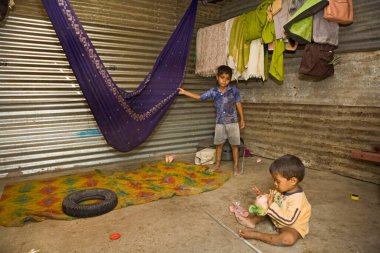 Ahmedabad, Gujarat, Hindistan 'daki bir inşaat sahasında derme çatma çarşafta oturan küçük kardeşler. 