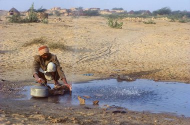 Sızdıran bir borudan su küçük bir boru kullanılarak toplanır ve tencere adam doldurulur; Batı Rajasthan; Hindistan;