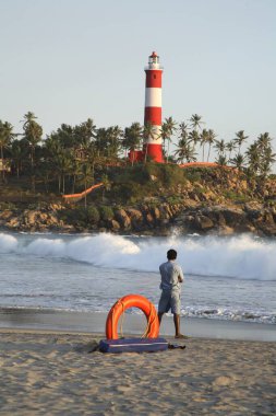 Kovalam beach and light house ; orange life guard ring with life guard watching waves ; Thiruvananthapuram District ; Kerala ; India clipart