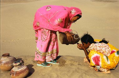 Deri çantadan su döken kadın susuzluğunu gidermek için başka bir kadına su veriyor, Khuhri, Jaisalmer, Rajasthan, Hindistan 