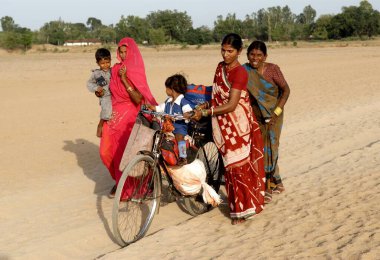 Çocuklarıyla yürüyen ve bisikletle yük taşıyan kadınlar, Garwa ve Latehar, Jharkhand, Hindistan 