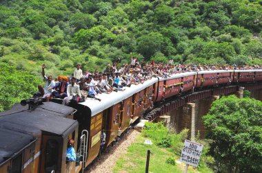 Köprüde giden trenin çatısında seyahat ederken risk alan insanlar; Rajasthan; Hindistan