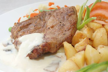 Yiyecek, ızgara domuz filetosu baharatlı patates, haşlanmış sebze (havuç, Fransız fasulyesi, karnabahar ve taze bezelye) ve domates ve pırasa ile süslenmiş mantar sosu ile servis edilir.