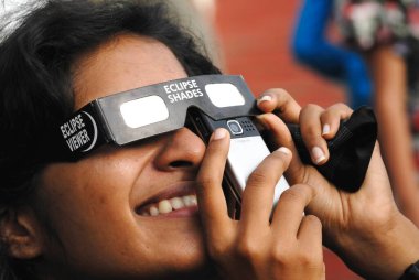 Cep telefonuyla fotoğraf çeken ve kısmi güneş tutulmasını izleyen genç bir kız 1 Ağustos 2008 'de Bombay Mumbai, Maharashtra, Hindistan' da koruma filtresi takıyor.  