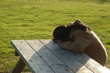 Hintli kadın bankta oturuyor ve başını masaya yaslıyor.