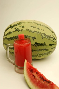 Fruits ; One full watermelon with light and dark green stripes and one cut slice showing red watery pulp and black seeds with glass of melon juice  ; Pune ;  Maharashtra ; India clipart