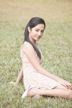 Çimenlerde oturan çekici bir kızın portresi. 