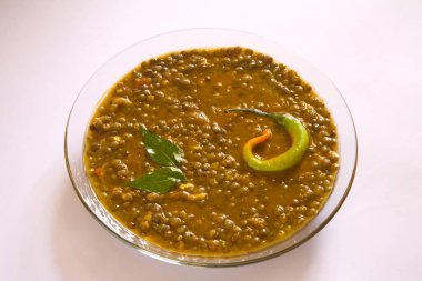 Indian masoor dal  red gram lentil soup garnish with curry leaves and chilli in glass bowl on white background