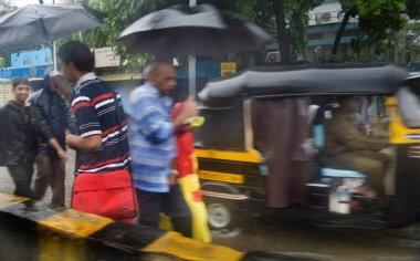 Muson yağmurları, ellerinde şemsiyelerle su dolu yolda yürüyen yayalar Mumbai Bombay, Maharashtra, Hindistan 