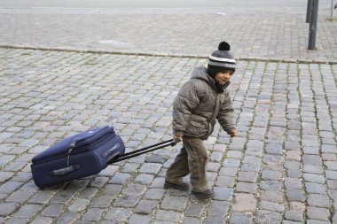 Kışlık giysiler içinde koyu mavi valiz taşıyan dört yaşında küçük bir çocuk. 
