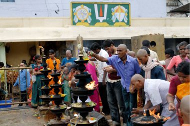 Devotees worshipping and offering coconut; camphor and flowers to Lord Venkateshwara (Balaji) in front of the huge oil lamps  at Tirumala temple; Tirupati, Andhra Pradesh, India  clipart