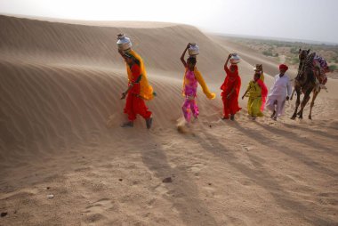 Kadınlar çölde deve adam, Jaisalmer, Rajasthan, Hindistan ile yürüyorlar. 