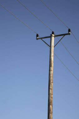 Mavi gökyüzüne karşı elektrik kabloları olan tahta elektrik direkleri; İsveç