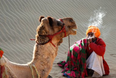 Camel and man smoking in desert in Khuri Khuhri, Jaisalmer, Rajasthan, India   clipart