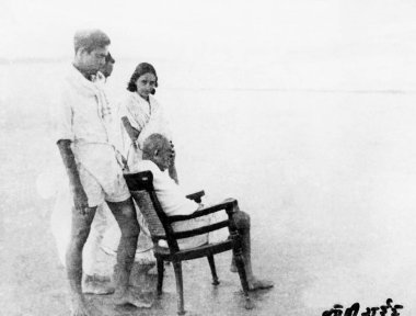 Mahatma Gandhi, sitting in a chair Juhu Beach, Mumbai, with people around him, May 1944, India   clipart