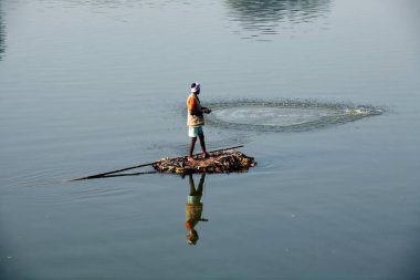 Sangli, Maharashtra, Hindistan 'da Krishna nehrinde balık yakalamak için balıkçı ağlarını attığı derme çatma bir tekneyle Haripur köyünden bir balıkçı.