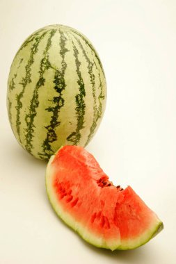 Fruits ; One full watermelon with light and dark green stripes and one cut slice showing red watery pulp with black seeds  ; Pune ;  Maharashtra ; India clipart