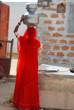Kapısında su kabı olan kadın, Jaisalmer, Rajasthan, Hindistan 