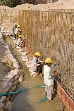 İnşaat işçileri levhayı çimento beton karışımıyla doldurmak için demir bir çerçeve üzerinde çalışıyorlar, Ahmedabad, Gujarat, Hindistan 