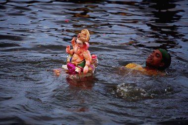 Idol of Lord Ganesha ganpati Hindu deity being immersed in Powai lake ; Bombay Mumbai ; Maharashtra ; India clipart