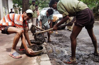 Kiralık işçiler Bombay Mumbai, Maharashtra, Hindistan yolundaki çöpleri ve çamuru temizliyor. 